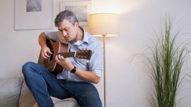 Gitar ilhamı. Melodi çalışması. Odaklanmış yetenekli bir sanatçı kanepeye oturmuş ev fotokopisinde akustik enstrüman çalıyor..