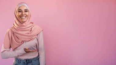Tavsiye edilen insanlar. Reklam arkaplanı. Pembe üzerine izole edilmiş metin için boş alan sunan tesettürlü mutlu kadın..
