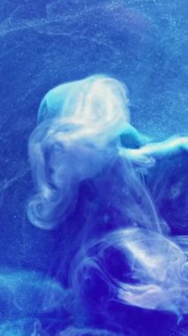 Dikey video. Mürekkep suyu. Boya sıçraması. Su altı patlaması. Mavi renkli, parlak, parıltılı duman bulutlu hareket soyut sanat arkaplanı.