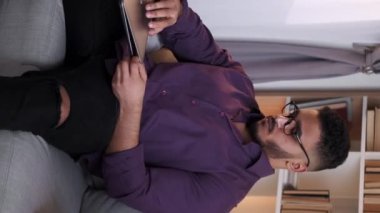 Dikey video. Mesafe öğrenme. Online eğitim. Uzaktan çalışma. Modern oturma odasındaki koltukta dizüstü bilgisayarla çalışan kendine güvenen zeki bir adam..