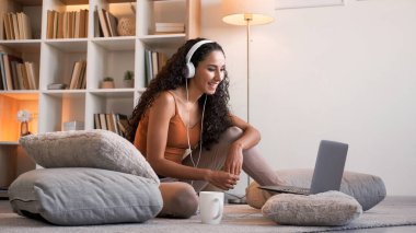 Görüntülü konuşma. Sanal iletişim. Rahatlamış, kulaklıklı, dizüstü bilgisayarlı bir kız. Açık ev iç mekanında, boş alanlı online sohbetin keyfini çıkarıyor..