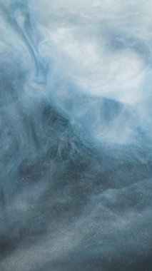 Dikey video. Parıldayan sis bulutu. Mürekkep suyu. Ruhsal aura. Mavi renkli duman yüzen parlak tanecikler soyut sanat arkaplanı dokusu.