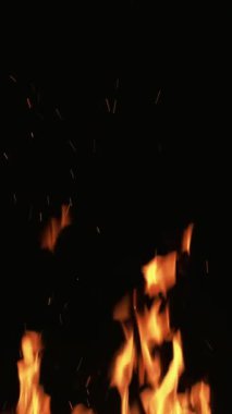 Dikey video. Yangın arka planı. Siyah üzerine alev. Turuncu renkli ışık yanan şömine ısısı karanlık gece boşluğunda hareket kıvılcımına neden olur..