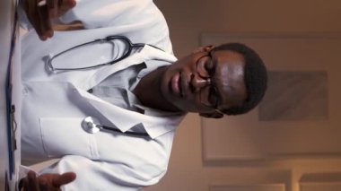 Dikey video. Tıbbi danışmanlık. Çevrimiçi doktor. Klinik tele-sağlık. Şaşkın erkek doktor hasta teşhisi üzerinde çalışırken omuz silkiyor..