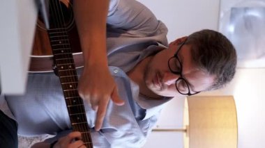 Dikey video. Gitar dersi. Müzik öğretmeni. İnternetteki konferans. Evde masadaki laptopta akustik enstrüman çalmayı açıklayan sıradan bir adamdan esinlendim..