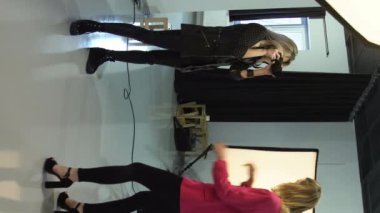 Dikey video. Kuliste moda. Kıyafet fotoğrafçılığı. Kadın fotoğrafçı profesyonel ekipman kullanıyor. Fotoğraf çekiyor. Güzel bir model..