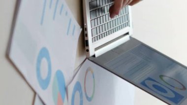Dikey video. Ofis işleri. İş analizi. Erkek ve kadın iş arkadaşları, iş yerlerindeki istatistik veri raporlarıyla birlikte masadaki dizüstü bilgisayarlarında yazı yazıyorlar..