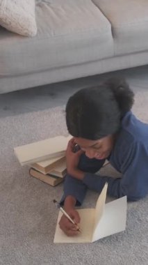 Dikey video. Yaratıcı yazar. Günlük boş zaman. Düşünceli hayalperest, mutlu, genç yazar kadının evdeki oturma odasındaki halının üzerine not almasına ilham kaynağı oldu..