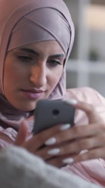 Dikey video. Spam mesajı. İnternet zorbalığı. Sinirli, huysuz, tesettürlü, telefonda mesaj atan kadın iletişim sorunu yüzünden üzgün..