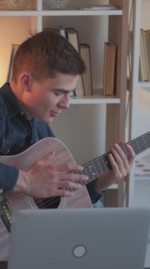 Dikey video. Çevrimiçi müzik dersi. Gitar dersi. Uzaktan eğitim. Evdeki dizüstü bilgisayar konferansında telli çalgılar dersi veren adam..