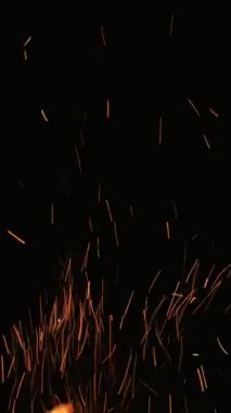 Dikey video. Ateş kıvılcımları. Siyah üzerine alev. Alev alev yanan. Işıldayan turuncu ışık parıltıları, karanlık gecelerde parlayan, soyut bir arka planda parlıyor..