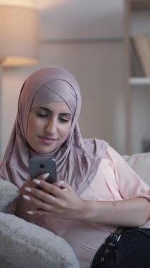 Dikey video. Gezici eğlence. Telefon taraması. Yurt içi istirahat. İnternette internette sörf yapan rahat bir kadın akıllı telefonda rahat bir kanepede, oturma odasında..