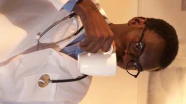 Dikey video. Doktor molası. Gece vardiyası. Meraklı, beyaz önlüklü, elinde kupayla TV 'de film izleyen, çay içen ciddi bir erkek doktor..