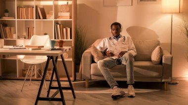 Doktor Leisure. Müzik dinleniyor. Gevşemeyi bırak. Yorgun erkek hekim, kulaklıkla kulaklıkla kulaklığı dinlemekten keyif alıyor modern iç mekandaki koltukta fotokopi uzayı ile..