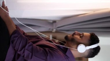 Dikey video. Müzik uygulaması. Sabah çalma listesi. Hafta sonu ilhamı. Rahatlamış adam kulaklıkla telefon dinlemekten zevk alıyor. Evde bedava kahve içiyor..