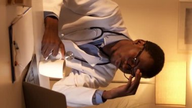 Dikey video. Çok çalışan doktor. Gece vardiyası yorgunluğu. Yorgun erkek doktor internetten internetten internet izleyerek kahve içiyor..