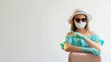 Pandemik tatil. Yolculuk koruma altında. Maskeli bir kız. Yazlık eldiven giyip, beyaz arka planda izole edilmiş görünmez bir şeyi gösteren boş bir yeri işaret ediyor..