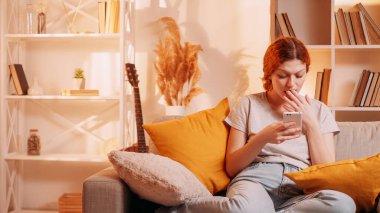 Şok edici bir haber. Gezici sürpriz. Şaşırmış bir kadın telefon interneti kullanıyor sosyal medyayı okuyor evdeki kanepede fotokopi alanı olan sosyal medya okuyor..
