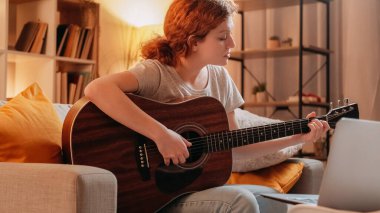 Gitar dersi. Çevrimiçi akustik eğitim. Profesyonel esinlenilmiş müzisyen kadın evde dizüstü bilgisayarda telli çalgı çalmayı öğretiyor..
