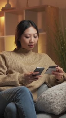 Dikey video. Mobil bankacılık. Çevrimiçi ödeme. İnternet alışverişi. Rahatlamış bir kadın kredi kartı ve telefon kullanıyor..