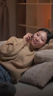 Dikey video. Telefon var. İyi akşamlar. Mobil iletişim. Rahatlamış, gülümseyen bir kadın. Hoş sohbetin tadını çıkarıyor..