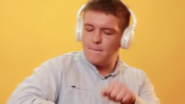Müzik eğlenceli. DJ tarzı. İnsanların eğlencesi. Şişman, şişman bir adam, sarı arka planda izole edilmiş beyaz kulaklıklarda ateşli müzik dinlerken ritmik bir şekilde şarkı söylüyor..