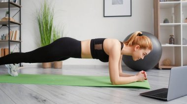 Online eğitim. Sabah sporu. Denge egzersizi. Sağlıklı bir yaşam tarzı. Yoga minderinin üzerinde dizüstü bilgisayarı olan sağlıklı bir kadın giysisi..