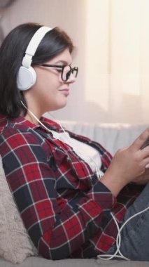 Dikey video. Mobil müzik. Şarkı dinlemede. Gadget 'ın boş vakti. Kulaklıklı tatmin olmuş bir kadın evdeki rahat koltukta telefon çalma listesinin keyfini çıkarıyor..