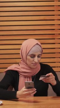 Dikey video. Çevrimiçi ödeme. Cep telefonu cüzdanı. Tesettürlü güzel bir kadın kredi kartıyla kahve siparişi veriyor..
