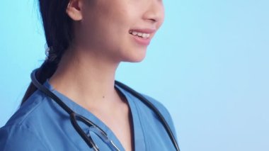 Gülümseyen doktor. Sağlık çalışanı. Dost canlısı, şefkatli kadın cerrah ayakta durup sağlık hizmetleri hastane üniforması mavi arka plan veriyor..