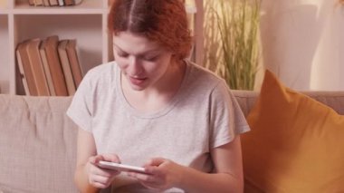 Telefon şakası. Oyun eğlencesi. Mobil cihazlı heyecanlı kadın video siber spor ev kanepede dinleniyor sıcak oturma odasında..