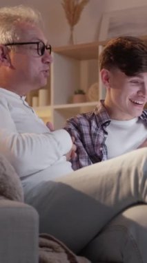 Dikey video. Aile eğlencesi. Ebeveynlik bağı. İnternet eğlencesi. Mutlu baba ve oğul dizüstü bilgisayarda film izliyor. Birlikte eğleniyorlar..