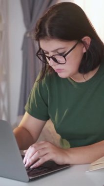 Dikey video. Son teslim tarihi. Bağımsız çalışmaktan yoruldum. Ciddi derecede mutsuz, aşırı çalışan bir kadın dizüstü bilgisayarda kompozisyon yazıyor. Evinin içinde oturuyor..