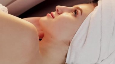 Dikey video. Günaydın güzellik. Tazelenmiş yüz. Sıvı cilt etkisi. Besleyici dokunuş. Havlu giymiş güzel bir kadın duştan sonra aynaya bakıyor..