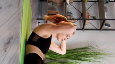 Dikey video. Fitness eğitimi. Ev antrenmanı. Güçlü vücut. Aktif yaşam tarzı. Aktif kıyafetli formalı bir kadın, iç mekandaki yoga minderinde karın kasları egzersizi yapıyor..