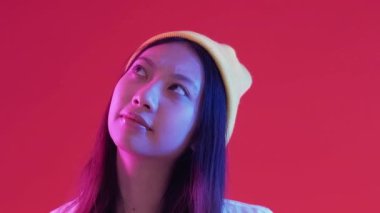 Fikir yürütme. Çözüm seçiliyor. Yeni nesil şaşkın kadın sorunlu sorulara cevap verirken mavi, neon ışıklı, kırmızı arka planda boş alan arıyor..