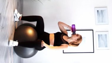 Dikey video. Fitness hidrasyonu. Su dengesi. Üretken bir egzersiz. Sağlıklı bir yaşam tarzı. Kadın, ışık odasının iç tarafındaki plastik şişeden içki içiyor..