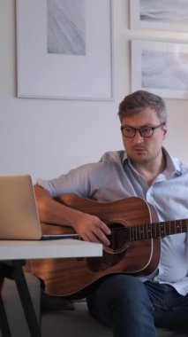 Dikey video. Müzik dersi. Akortlar çalışıyor. Çevrimiçi toplantı. Dizüstü bilgisayarda internet kursunda akustik gitar çalma kurallarını açıklayan profesyonel bir adamdan esinlendim..