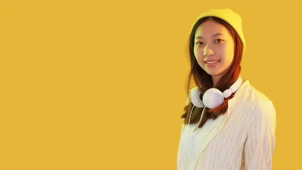 stock image Hipster girl. Street fashion. Color light friendly smiling teenager standing wearing headphones beanie isolated on yellow empty space background.