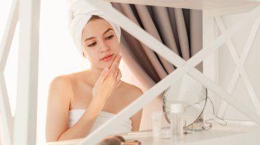 Kozmetik tedavi. Yüz bakımı. Duştan sonra şımarık. Pürüzsüz cilt güzelliği. Genç bayan mükemmel yüze nemlendirici krem sürüyor..