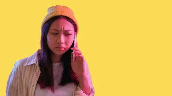 Stock image Phone problem. Mobile scam. Pink neon light skeptic frowning woman using gadget with bad connection isolated on yellow empty space background.