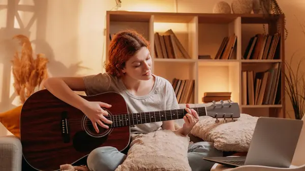 stock image Weekend guitar. Music vlog. Inspired musician woman enjoying playing acoustic instrument using laptop on couch at cozy home living room interior with free space.