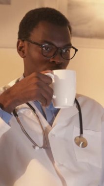 Dikey video. Doktor molası. Gece vardiyası. Meraklı, beyaz önlüklü, elinde kupayla TV 'de film izleyen, çay içen ciddi bir erkek doktor..