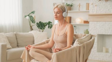 Ses meditasyonu. Huzurlu bir denge. Rahatlık ve rahatlık. Kulaklıklı rahat bir kadın koltukta rahat bir şekilde oturmuş evde mantra dinliyor..