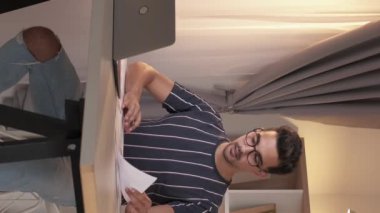 Dikey video. Mesafe çalışması. Rapor hazırlanıyor. Profesyonel bir adam iş evrakları üzerinde çalışıyor. Masasında dizüstü bilgisayarla ev içi ofis içinde oturuyor..