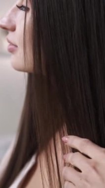 Dikey video. Saç bakımı. Ev rutini. Dişi kadın, pürüzsüz, kalın, parlak, sağlıklı, düz ve doğal ahşap taraklı telleri fırçalıyor..