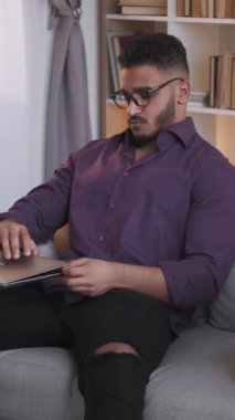 Dikey video. Mesafe öğrenme. Online eğitim. Uzaktan çalışma. Modern oturma odasındaki koltukta dizüstü bilgisayarla çalışan kendine güvenen zeki bir adam..