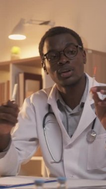 Dikey video. Enjeksiyon danışmanlığı. Eczacılık sınıfı. Çevrimiçi sağlık eğitimi. Beyaz önlüklü erkek doktor uyuşturucu şırıngasını karşılaştırma dersi veriyor..