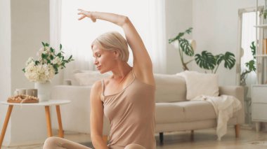 Pilates egzersizi. Esneme egzersizi. Sağlıklı bir sabah. Rahat aktif giyimli, formalı, rahat bir kadın evde, oturma odasında yan eğilme egzersizi yapıyor..