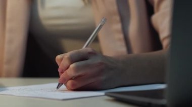 El yazısı. Çevrimiçi çalışma. Tanımlanamayan bir kadın kalemle sınava hazırlanıyor. Çalışma alanında dizüstü bilgisayarla üniversite için rapor hazırlıyor..